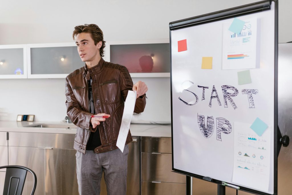 entrepreneur presents a startup idea next to a whiteboard with the word "start up" and various notes on funding in startup.