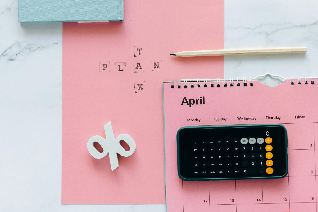 A calendar, calculator, and pen on pink paper. Symbolizing tax and funding in startups.